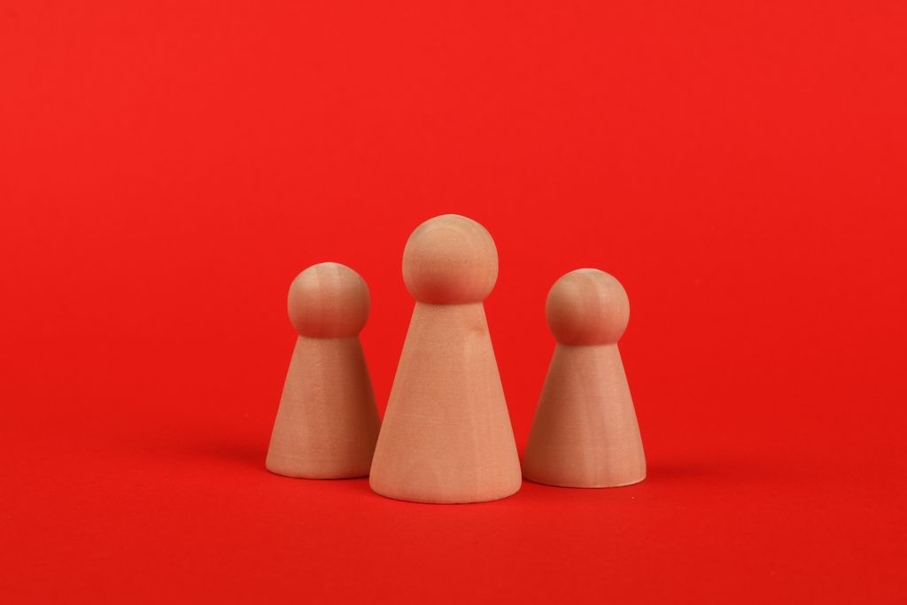 Three minimalist wooden figures on a bold red studio backdrop.